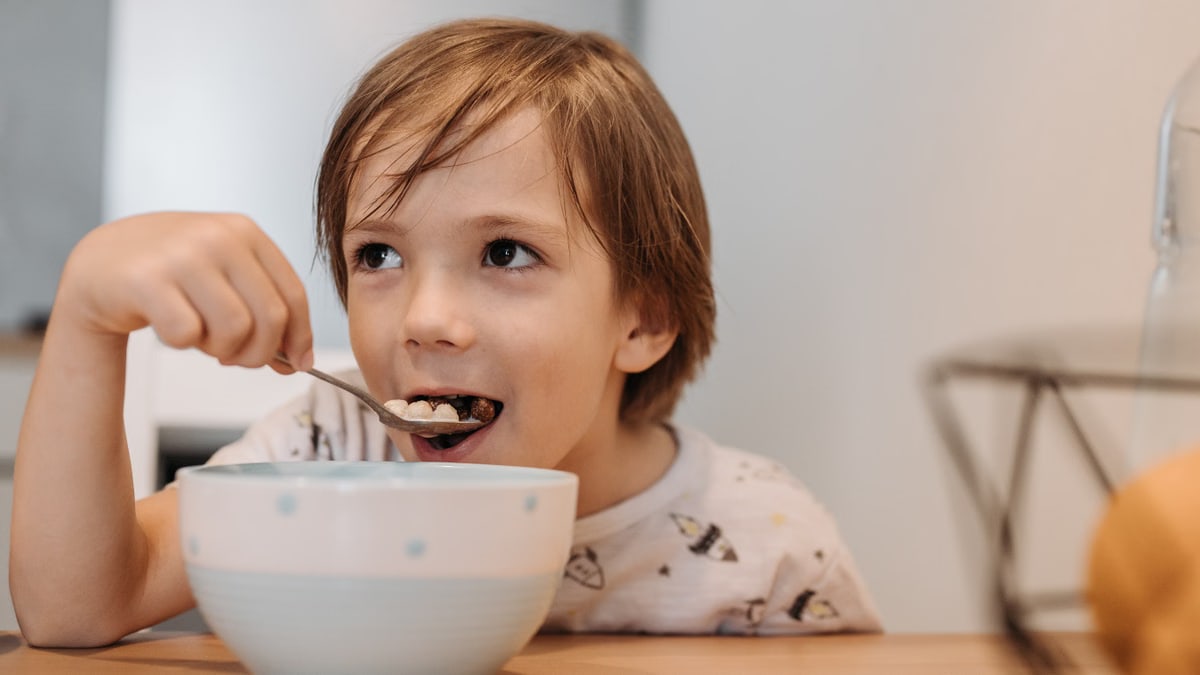 Adorable child enjoying cereal at breakfast indoors with a spoon.
